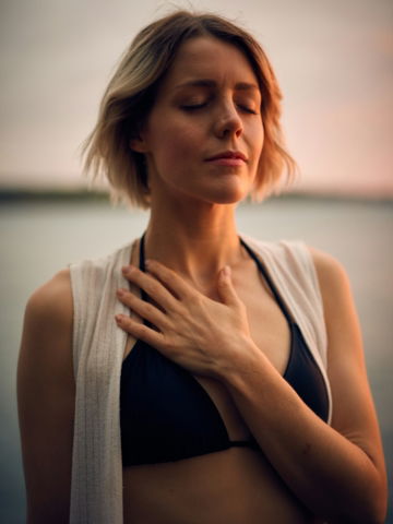 woman in white vest and black bikini with hand on chest
